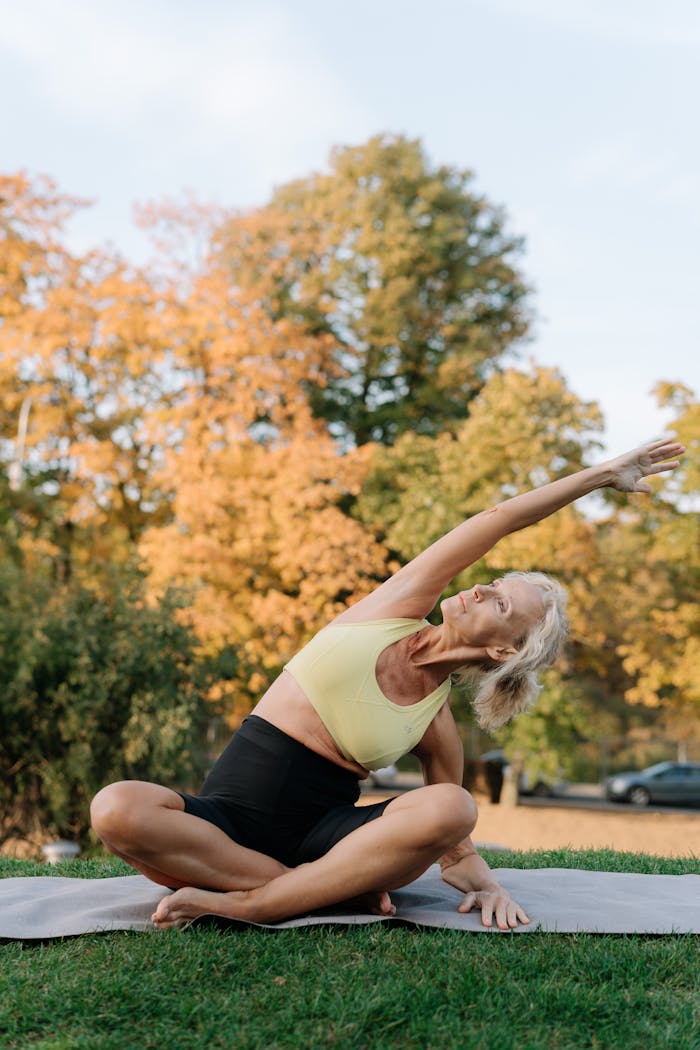 Elderly woman in sportswear stretching on a yoga mat in a park during fall.