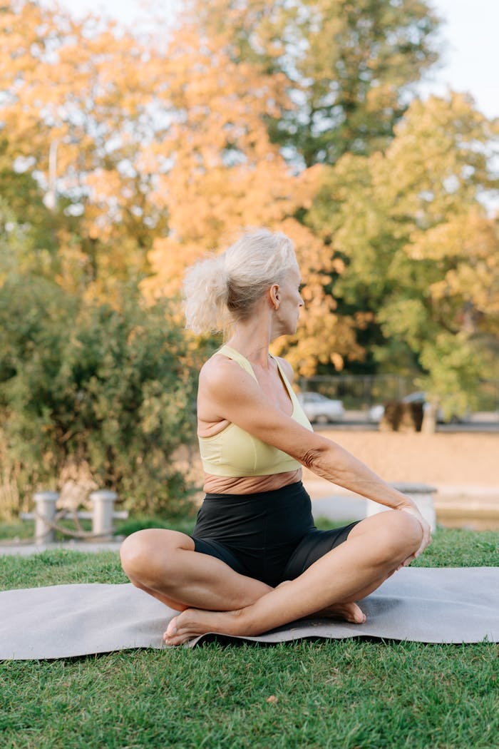 services-01 Senior woman in activewear sitting on yoga mat outdoors in autumn park.