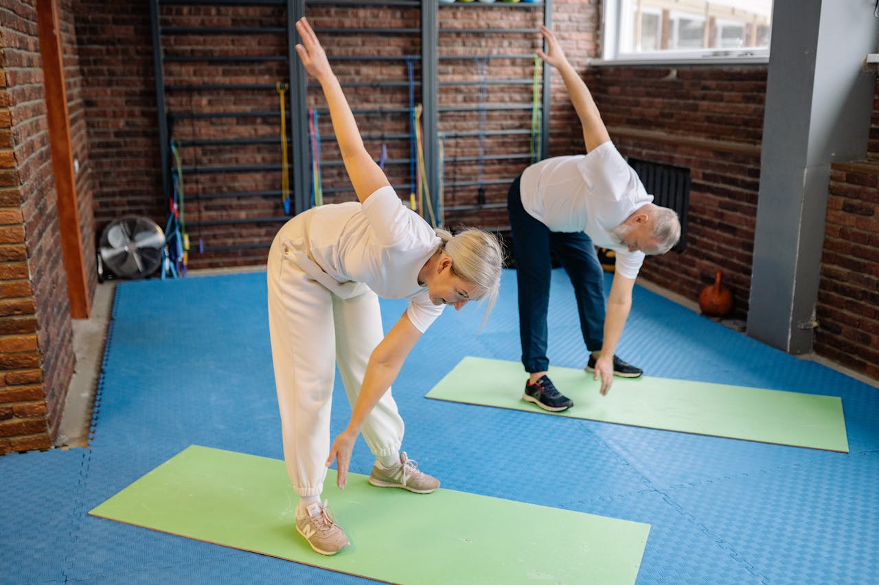 gallery-04 Active senior couple performing stretching exercises on mats in a modern fitness gym.