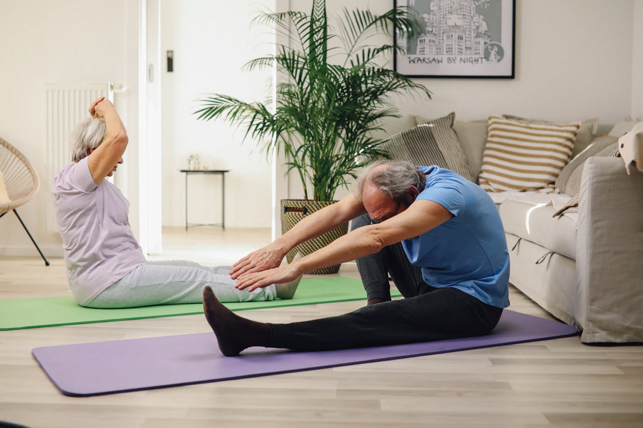 gallery-01 Elderly couple practicing yoga at home, promoting wellness and healthy lifestyle.