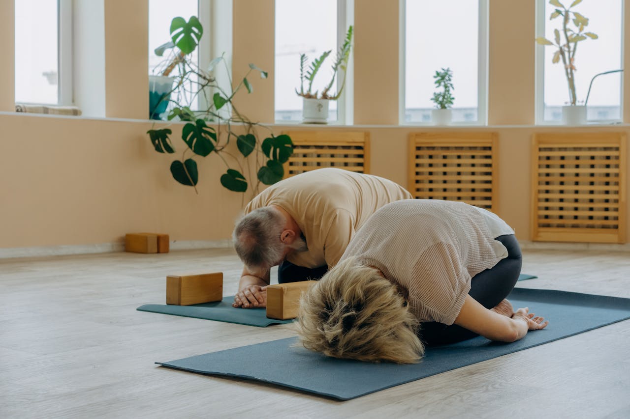 our-story Senior couple practicing yoga together indoors, focusing on stretching and wellness.