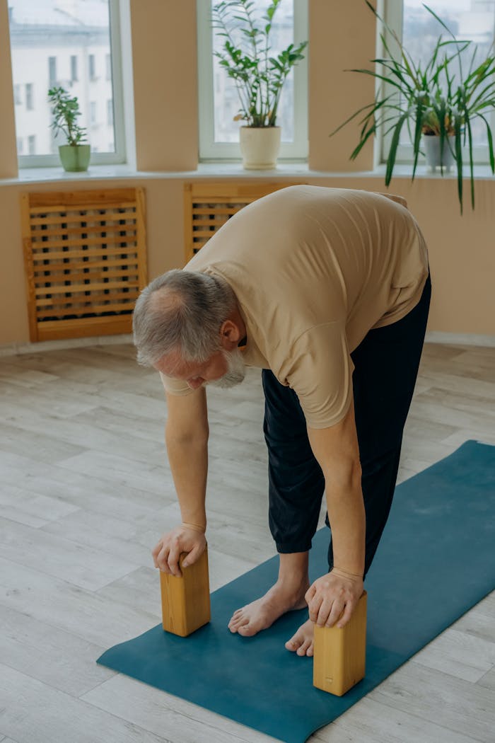 Elderly man stretching on a yoga mat using blocks for support in a cozy indoor setting.