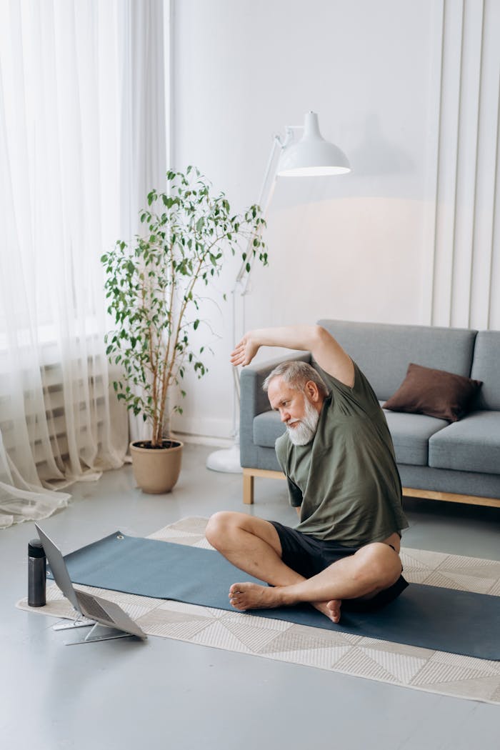 Elderly man doing yoga exercises on a mat in the living room, embracing a healthy lifestyle.
