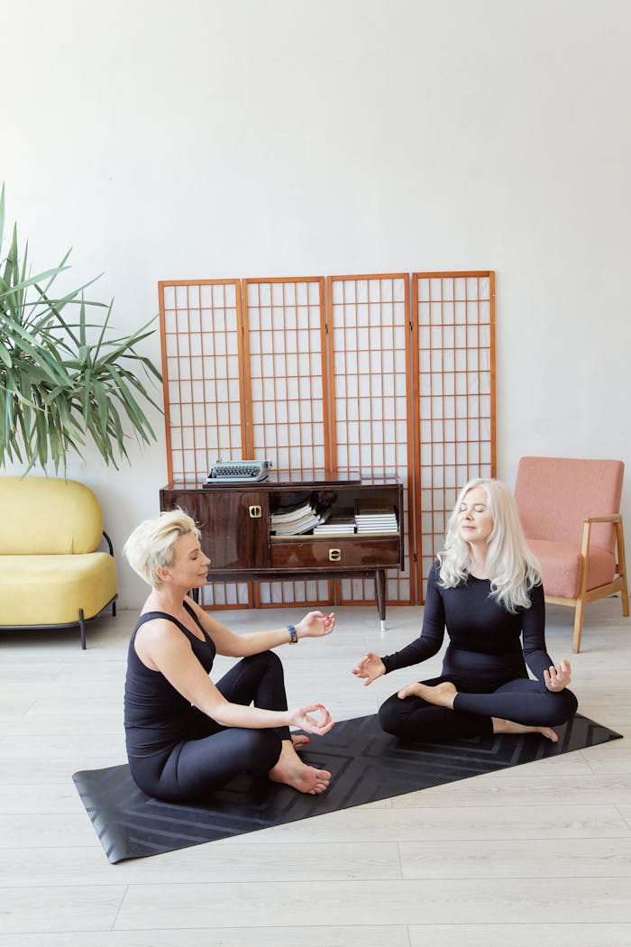 gallery-03 Two senior women practicing meditation on yoga mats in a calm indoor setting.