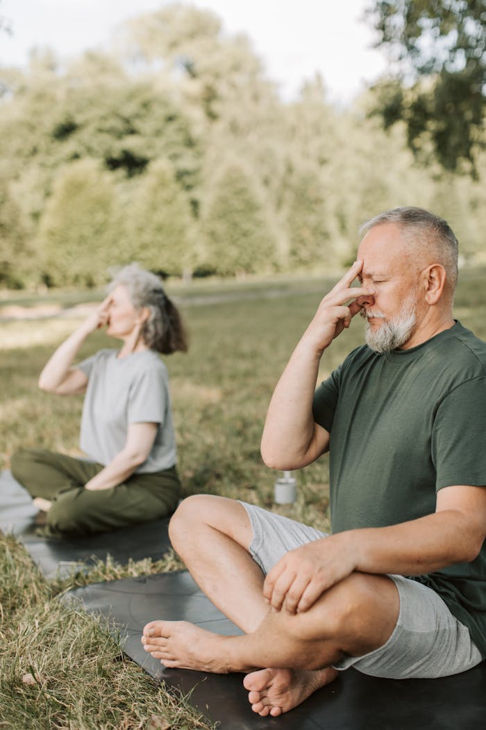 Elderly man and woman practicing yoga outdoors, promoting relaxation and healthy lifestyle.